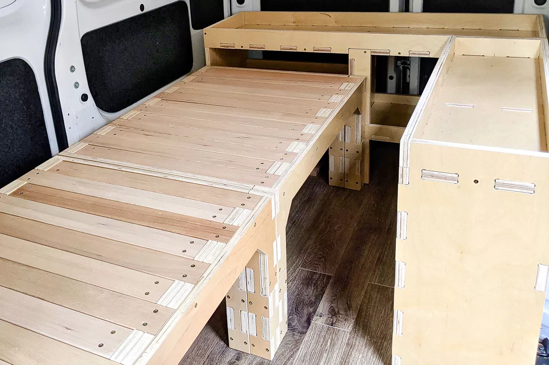 A wooden van camping kit with expanding bed and shelving inside a Nissan NV200.