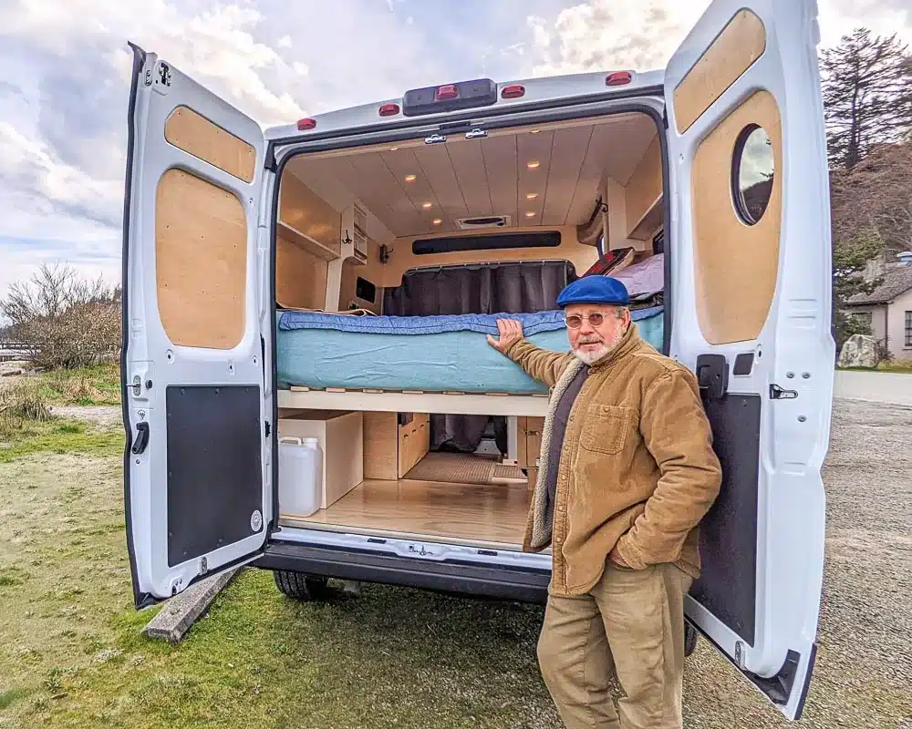 Man with his custom converted RAM ProMaster campervan with natural wood interior.